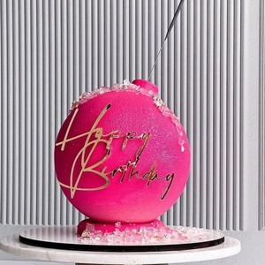 Detailed view of pink bomb-shaped birthday cake with golden Happy Birthday acrylic topper