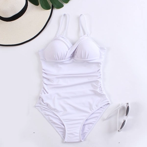 Flat lay of white one-piece swimsuit with ruched cups and cross straps on vacation background