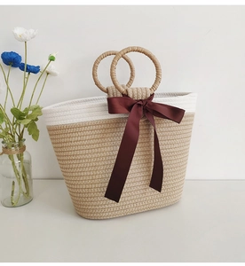 Detail of woven tote bag with round handles and a wine red ribbon bow accent