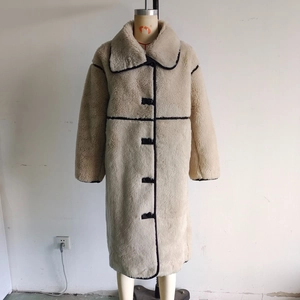 Dettaglio di un cappotto lungo in peluche con ampi revers e bordi neri a contrasto