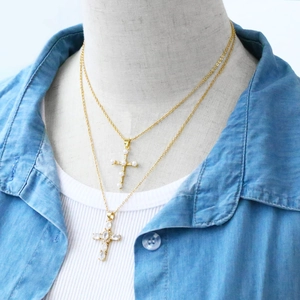 Close-up of layered gold necklaces featuring pearl and zircon cross pendants on a model