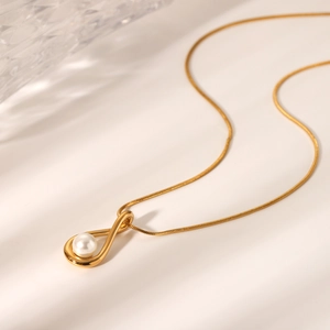 Detailed close-up of a gold hollow teardrop pendant with a white pearl on a fine chain