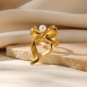 Detail of gold bow ring with center pearl on a textured stone and beige fabric backdrop