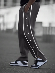 Side view of men's black snap button track pants with white side stripes in outdoor setting