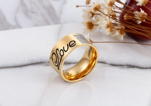 Macro shot of gold-plated wide ring featuring black Love script and cubic zirconia accents