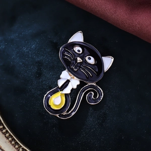 Detail of cute black cat brooch with enamel finish and white bow on velvet texture