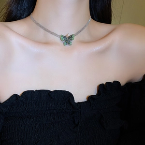 Close-up of green crystal butterfly pendant on a silver braided chain worn by model