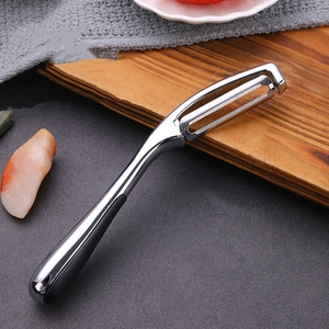 Detail of stainless steel peeler with black non-slip handle on a professional kitchen counter