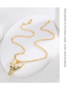 Detail of gold-plated bull head pendant with blue gemstone eyes and smooth metal finish