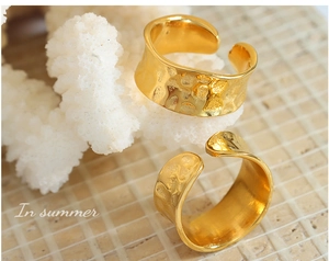 Detail of two golden hammered texture rings on white coral and beige brick background
