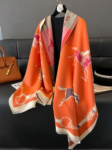 Orange thick double-sided horse print scarf with tassels displayed on a black sofa