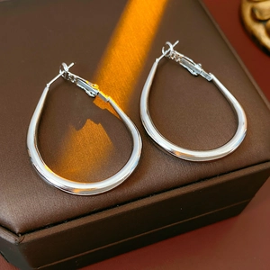 Detail of silver drop-shaped hoop earrings on a textured jewelry box with warm lighting