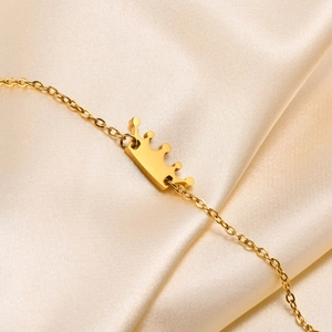 Detail of a golden crown pendant with delicate chain on a luxurious champagne silk background