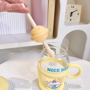 Close-up of glass cup with yellow silicone handle and planet-shaped tea infuser on straw