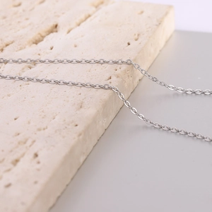 Close-up of a silver polished stainless steel necklace chain on a textured stone surface
