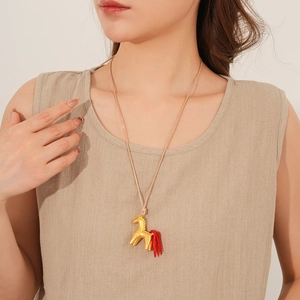 Detailed close-up of golden horse pendant necklace with red fringe on a beige rope cord