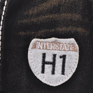 Close-up of Interstate H1 shield embroidery on washed black denim baseball cap fabric