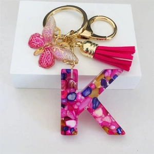 Detail of pink resin letter K keychain with butterfly charm and tassel on white base