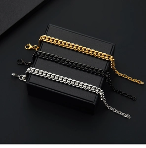 Three Cuban link bracelets in gold, black, and silver displayed on a gift box
