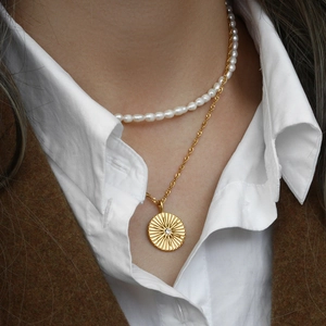 Dettaglio della collana con pendente a disco dorato con trama a raggiera e perle su modella