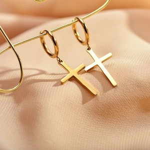 Golden stainless steel hoop earrings with cross pendants on pink silk background