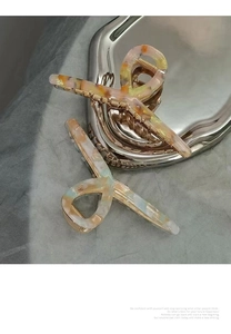 Detail of acetate hair claws with marble texture and golden metal spring on silver tray