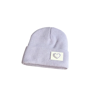 Close-up of a purple knitted beanie featuring a heart embroidery patch on the folded brim