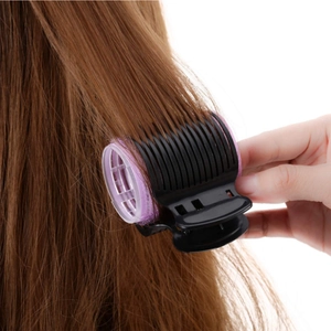 Close-up of pink hair roller with black clip showing styling detail and usage scene