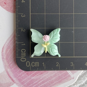 Macro shot of 3cm mint green resin butterfly accessory with pink rose on a cutting mat