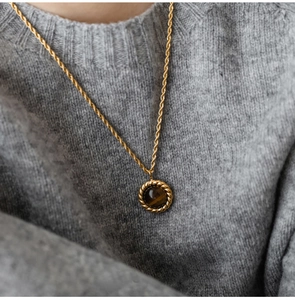 Detailed close-up of a golden rope chain necklace with a round tiger eye stone pendant