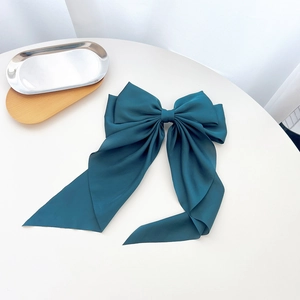 Detail of large dark green silk bow hairclip with long ribbons on a white surface
