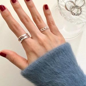Close-up of minimalist S925 silver wave and chain rings worn on a hand with blue sweater