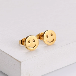 Macro detail of gold-plated stainless steel smiley face stud earrings on a white stand