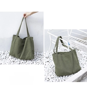 Detail of army green canvas tote bag displayed on white chair and pebbles background
