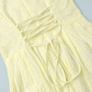 Macro shot of yellow cotton dress featuring floral embroidery and lace-up back detail