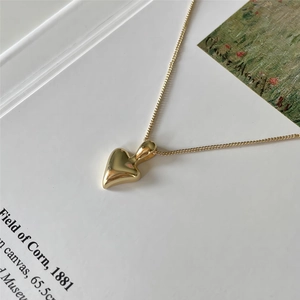 Artistic detail of a polished gold heart-shaped pendant necklace on a creative background