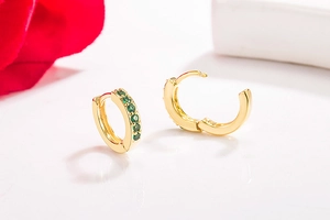 Detail of 14K gold plated earrings featuring green rhinestones on white reflective surface