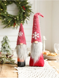 Close-up of red gnome bottle cover and plush doll with snowflakes in festive setting