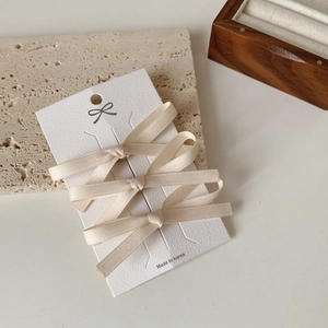 Gedetailleerd overzicht van beige zijden strik haarspelden set op een presentatiekaart