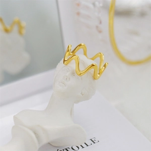 Artistic display of a gold wavy band ring styled as a crown on a white statuette