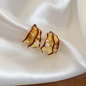 Detail of gold wavy earrings with red trim and pearls on white silk background
