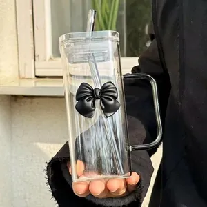 Detail of square glass cup with black bow, handle and straw in a sunlit hand