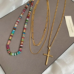 Detailed macro of layered gold cross pendant necklaces with multicolored beads and chains