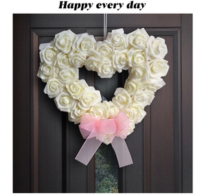 Détail d'une couronne de roses blanches en forme de cœur avec un nœud rose sur porte
