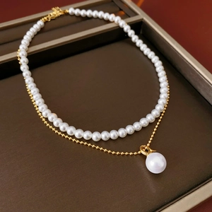 Detail of layered gold-plated necklace with white faux pearls on a brown display tray
