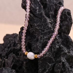 Macro detail of a purple crystal beaded necklace with a white pearl on volcanic rock