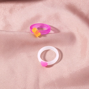 Detail of resin fruit rings with purple bear and pink heart on pink silk fabric