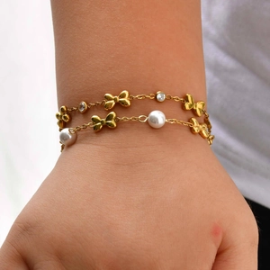 Detailed macro of gold-plated double-layer bracelet with bow charms and imitation pearls