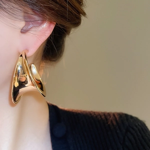 Close-up of model wearing chunky golden C-shaped hoop earrings with sculptural metal finish