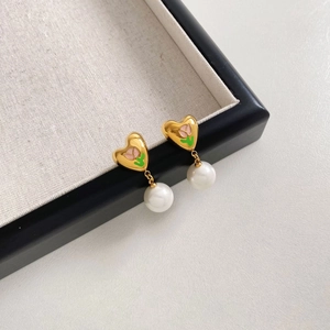 Détail de boucles d'oreilles cœur vintage avec émail tulipe et perle sur plateau lin